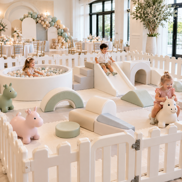 Soft play rental setup with white fence panels, foam climbing equipment, ball pit, animal hopper toys, and toddlers playing at an indoor event.