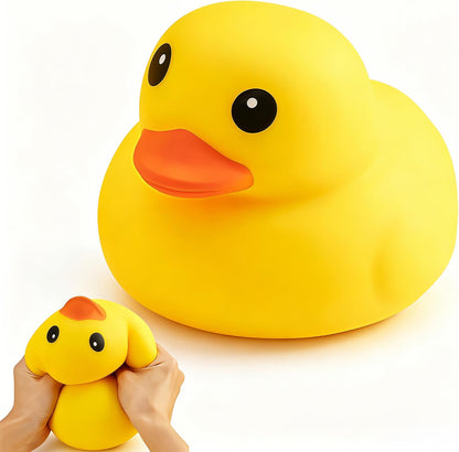 In the foreground, hands squeeze a smaller yellow squishy toy while in front sits the Okie Soft Play “Giant Yellow Duck Squishy – Flour-Filled TPR Fidget & Stress Relief Toy,” featuring a large, smooth yellow surface with hints of orange and an orange beak. Both ducks have wide, cartoonish eyes, set against a plain white background.