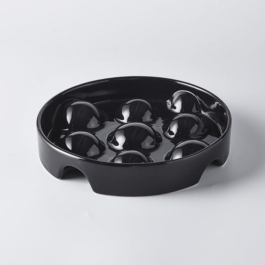 The OkiePaw Ceramic Slow Feeder Dog Bowl – 8.6 Inch from Okie Soft Play Store is a round black ceramic tray designed as a dog slow bowl, featuring nine raised domes inside arranged in a 3x3 grid pattern and two semi-circular notches on opposite sides of the rim.