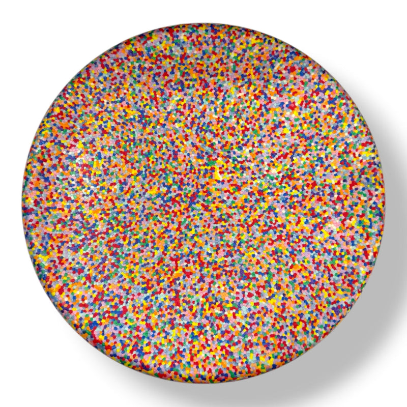 The Rainbow Balance Board for Kids by Okie Soft Play Store features a lively design with a dense pattern of colorful dots in red, yellow, blue, green, and purple on a white surface. This wobble board creates a vibrant, pointillist effect and casts a shadow to the right.